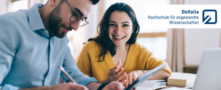 Ostfalia Advertisement: Pleased couple dressed in casual clothes writing notes in notebook while using tablet and sitting at table with laptop at home
